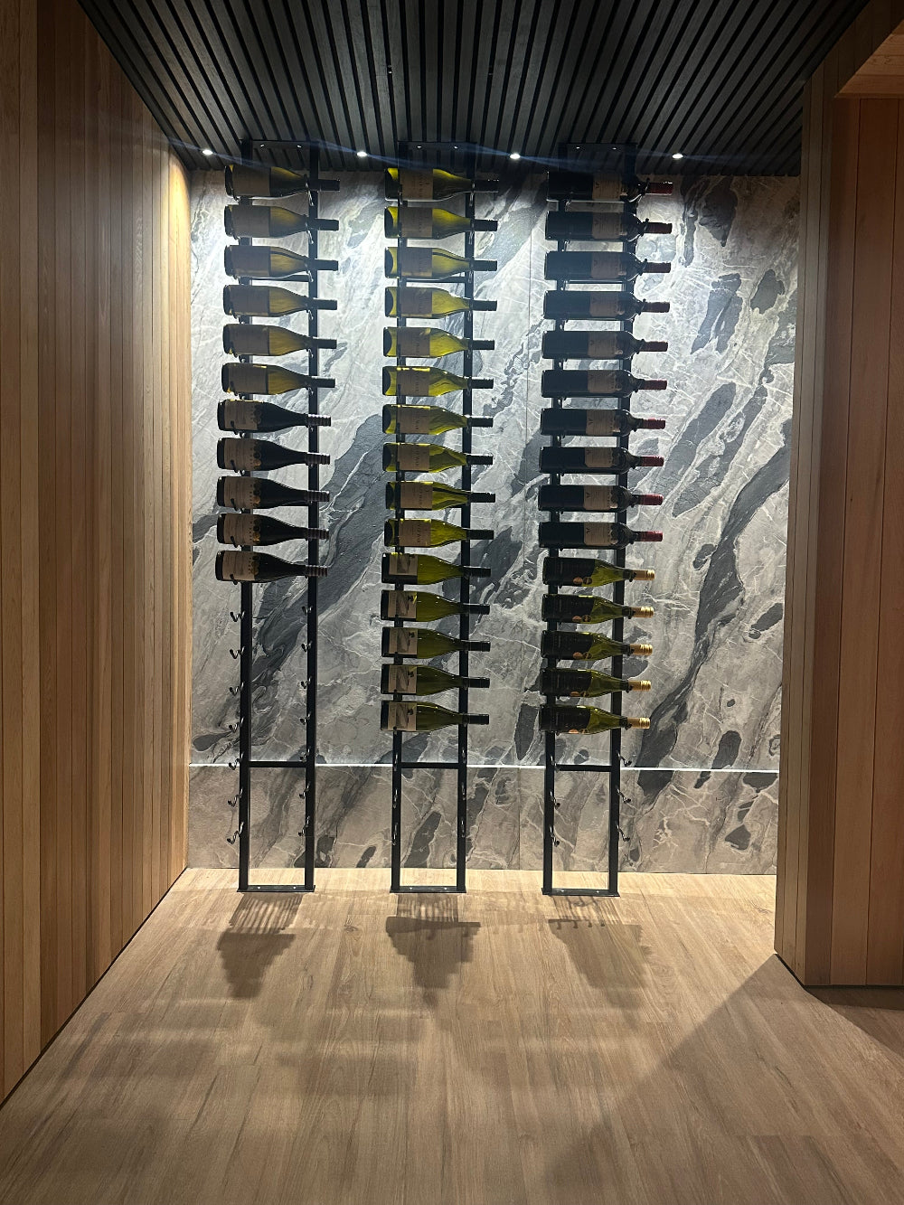 Wine bottles arranged on a metal rack in a modern wine cellar with marble walls.