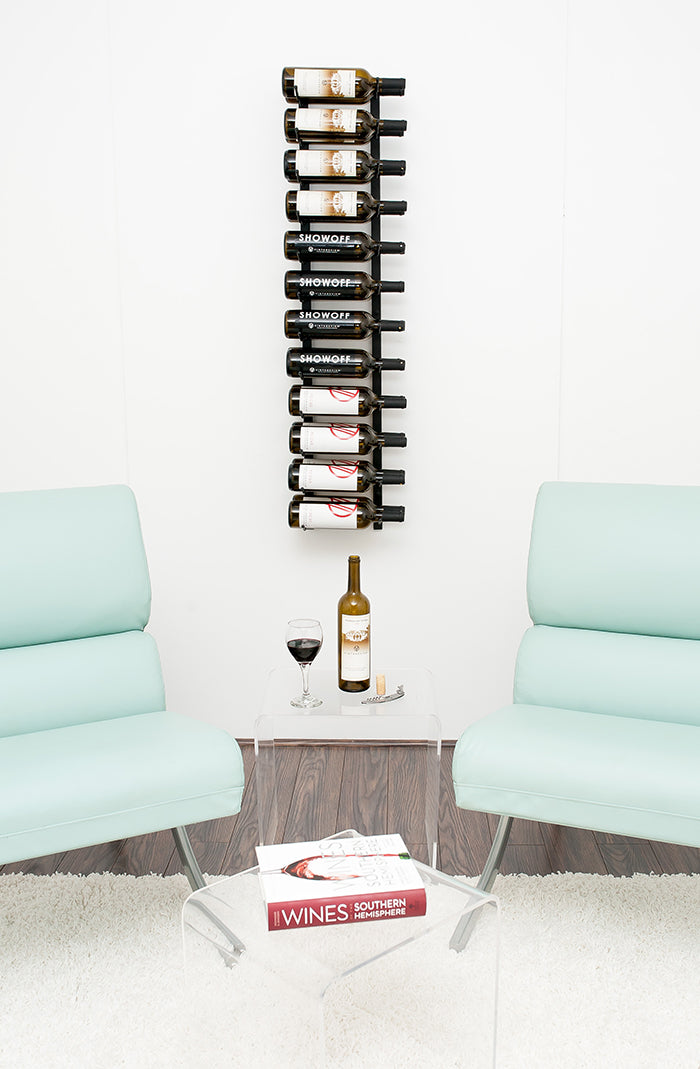 Black metal wine rack that is double depth on a wall with wine labels forward facing, two chairs on either side, small coffee table in the centre